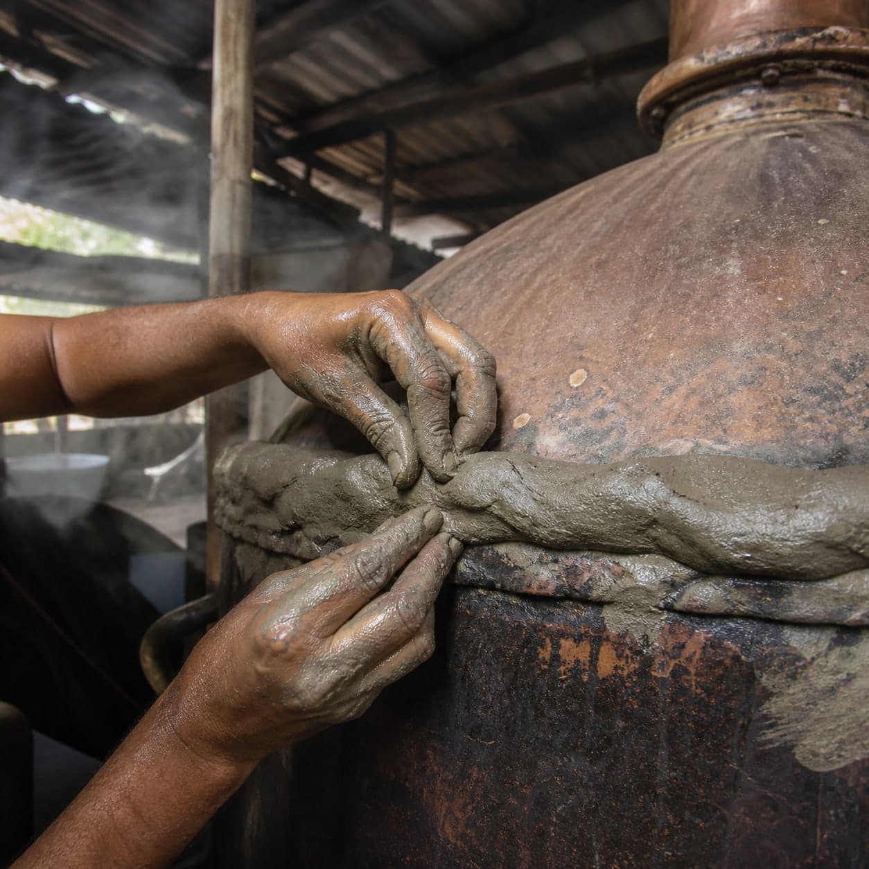 Hands sealing the copper lid of a deg with a rope of wet clay